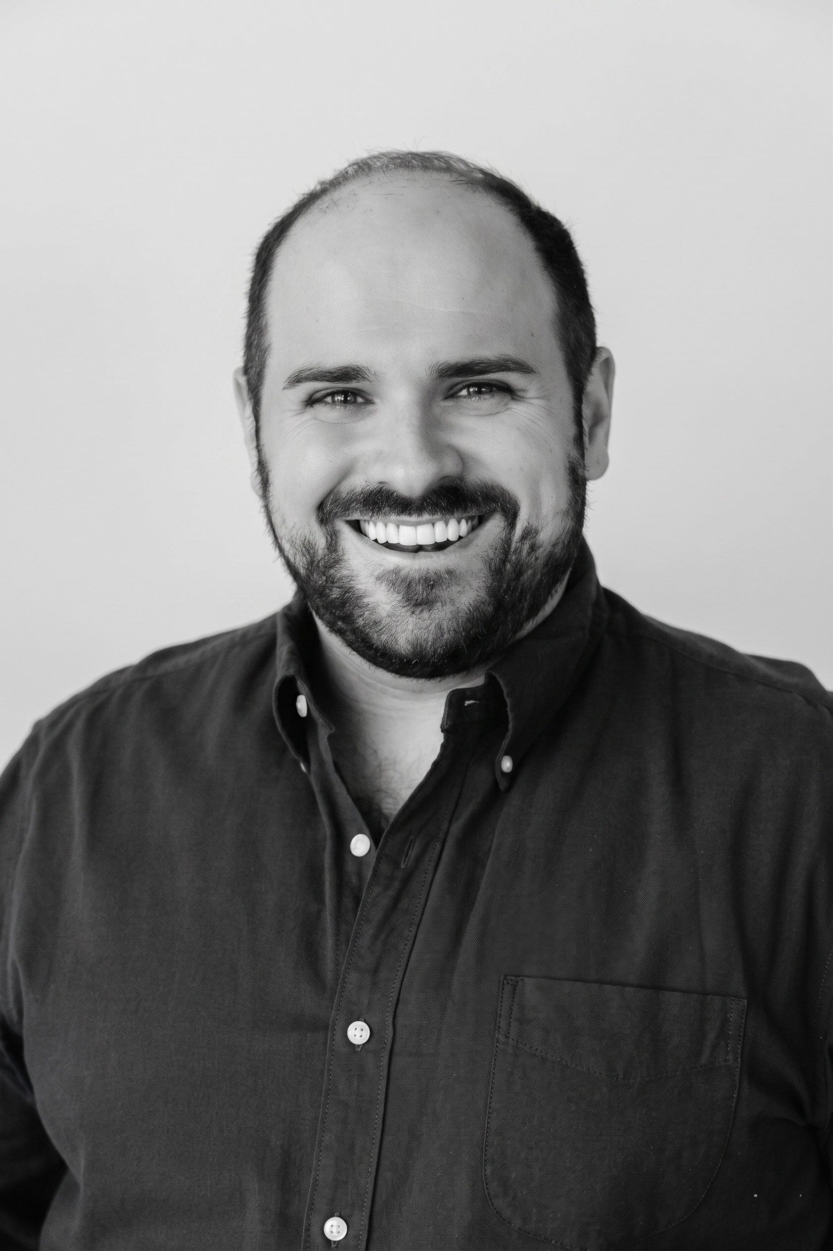Smiling man with a beard and dark shirt, facing forward with a neutral background.
